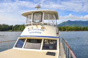 Front view of upper deck of luxury yacht with tree covered shore line and mountains in distance